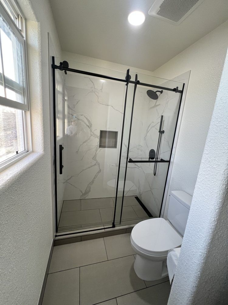 Modern bathroom with glass shower, tiled floor, window, and toilet in the foreground