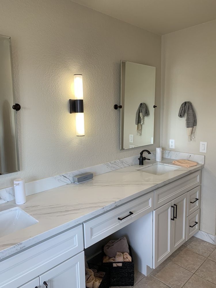 Modern bathroom vanity with double sinks, large mirror, wall sconce, and white cabinetry.