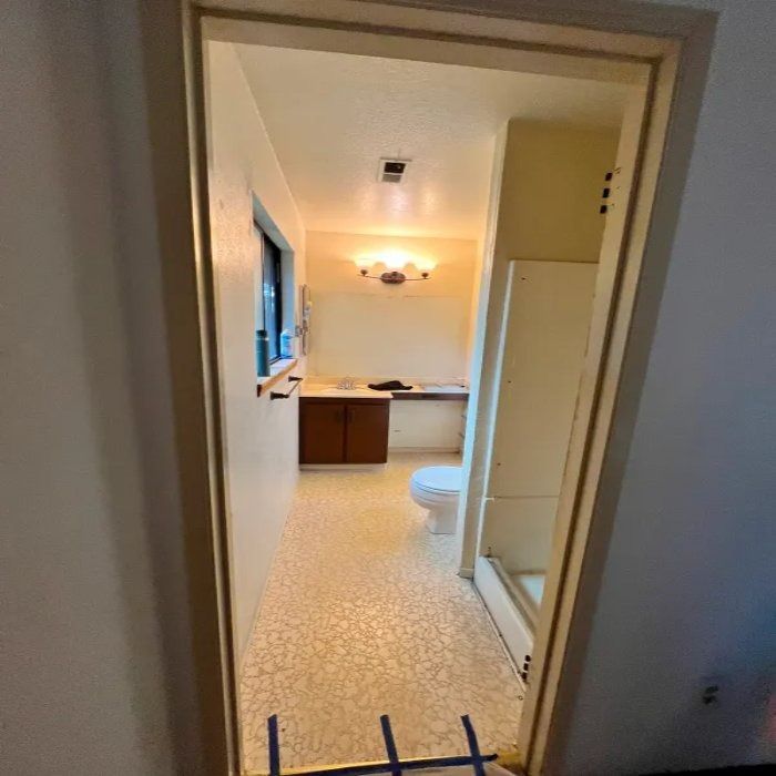 View through a doorway into a bathroom with a vanity, mirror light, shower stall, and patterned tile floor.