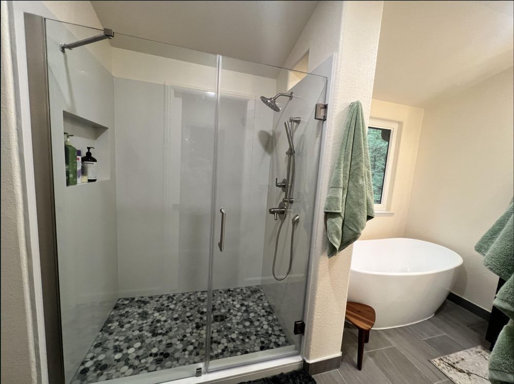 Modern bathroom with glass shower, pebble floor, and freestanding tub near a window