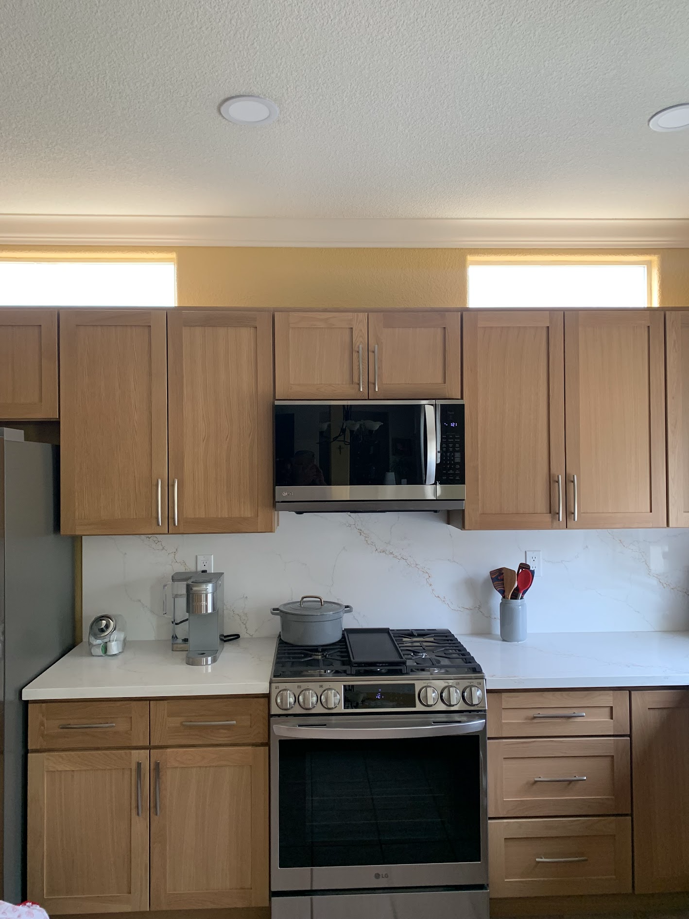 Kitchen with wooden cabinets, stainless stove and microwave, white countertop, and coffee maker on the left
