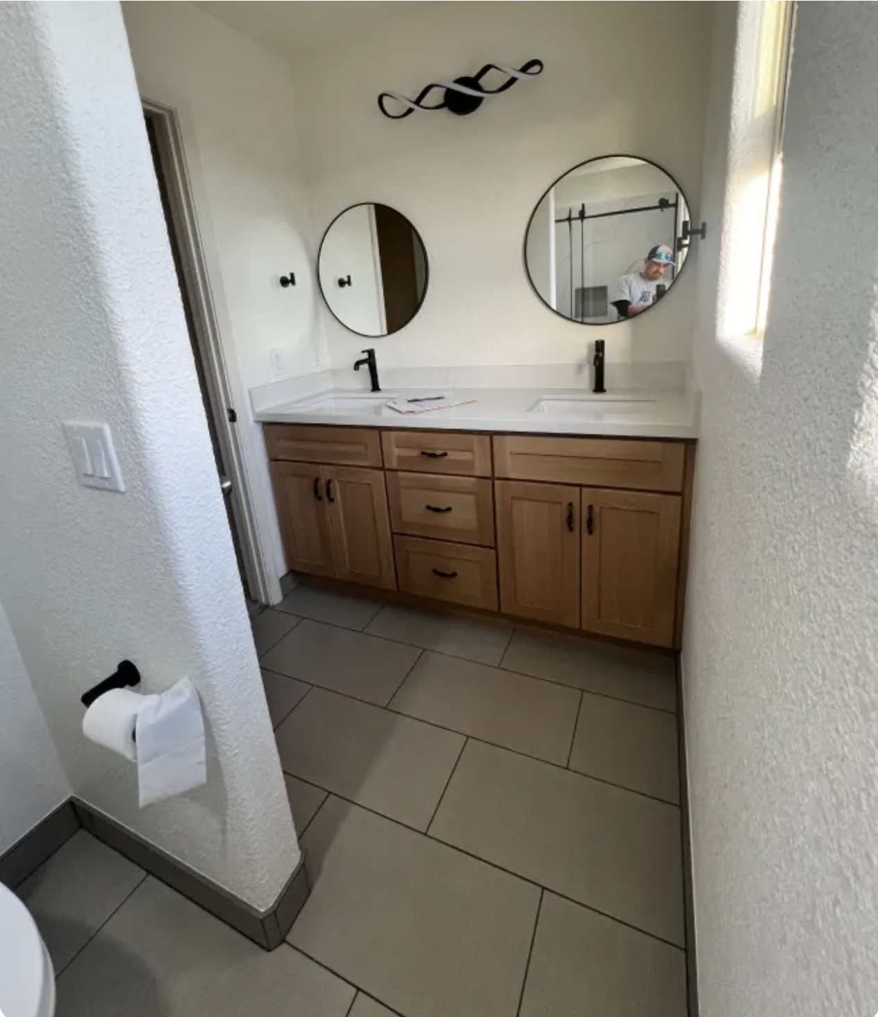 Small bathroom vanity with double sinks, round mirrors, and a towel holder beside a tiled floor.