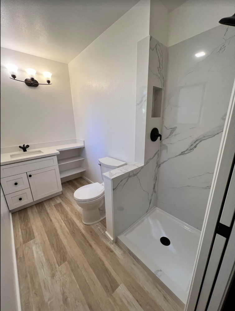 Modern bathroom with white marble shower, toilet, vanity, and light wood flooring