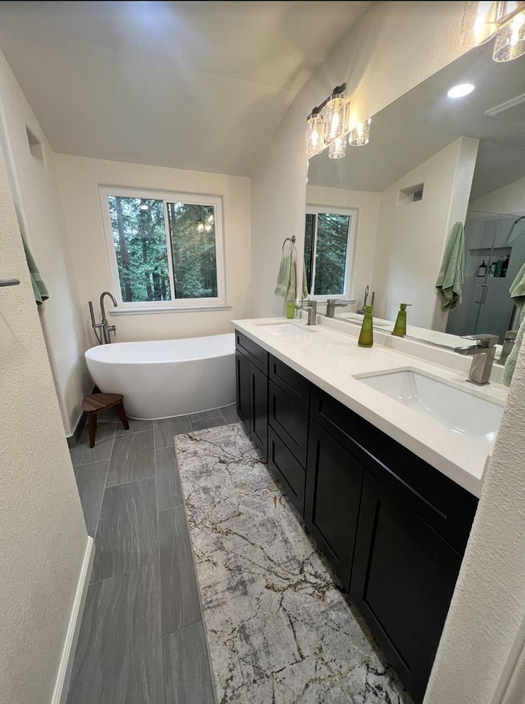 Bright modern bathroom with freestanding tub, long vanity, large mirror, and window view