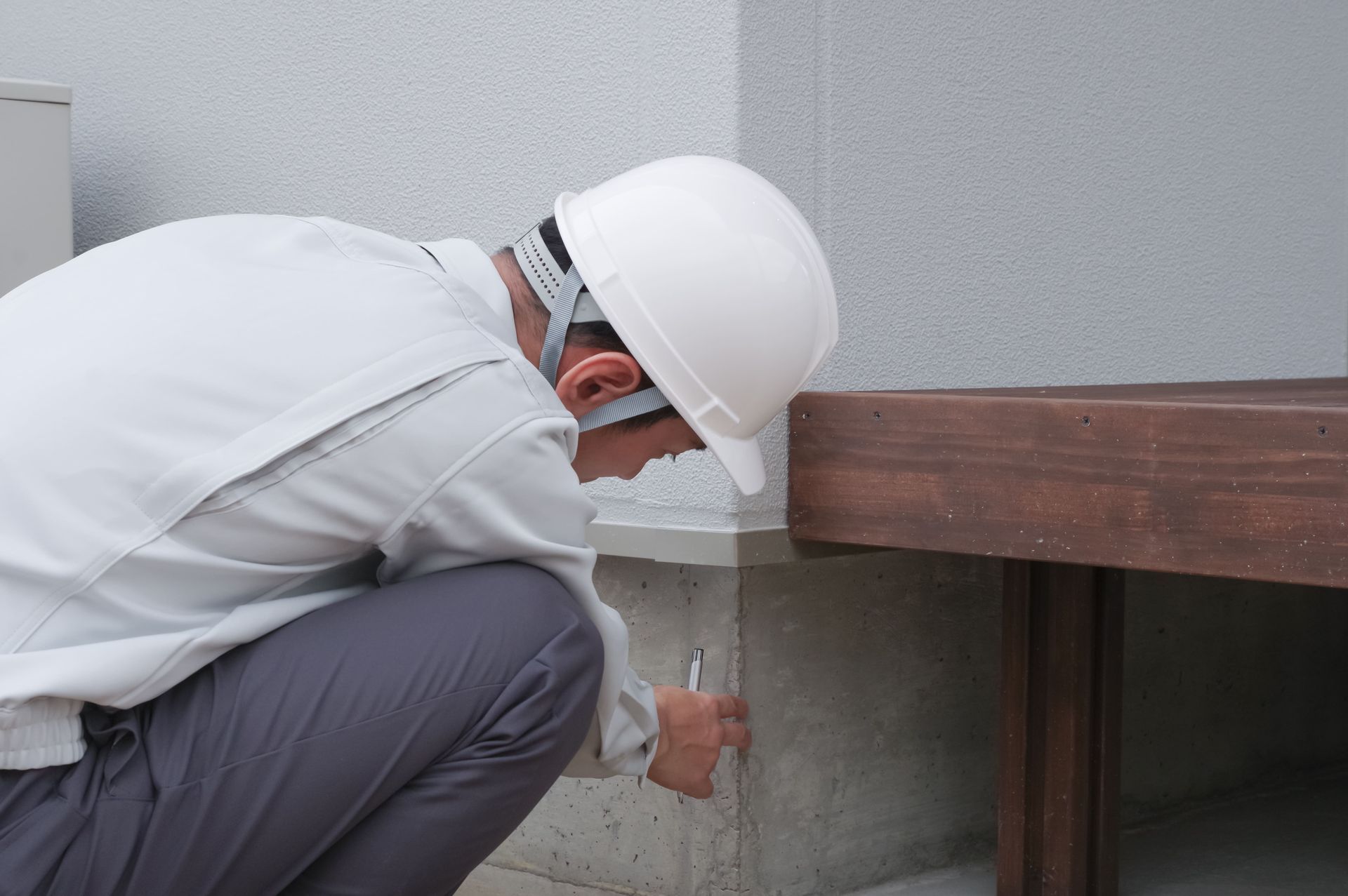 Worker in white hard hat inspecting a wooden beam under a building