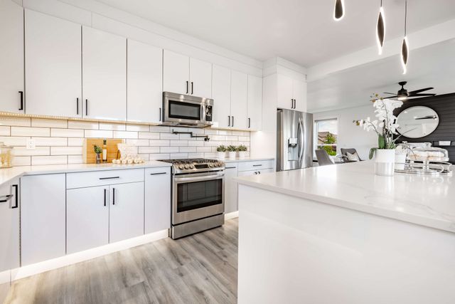 Bright white modern kitchen with stainless steel appliances, island, and gray wood flooring