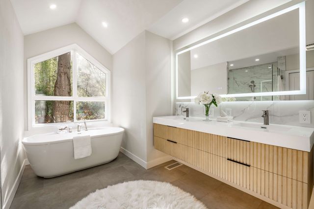 Bright modern bathroom with freestanding tub, double vanity, large mirror, and skylight windows