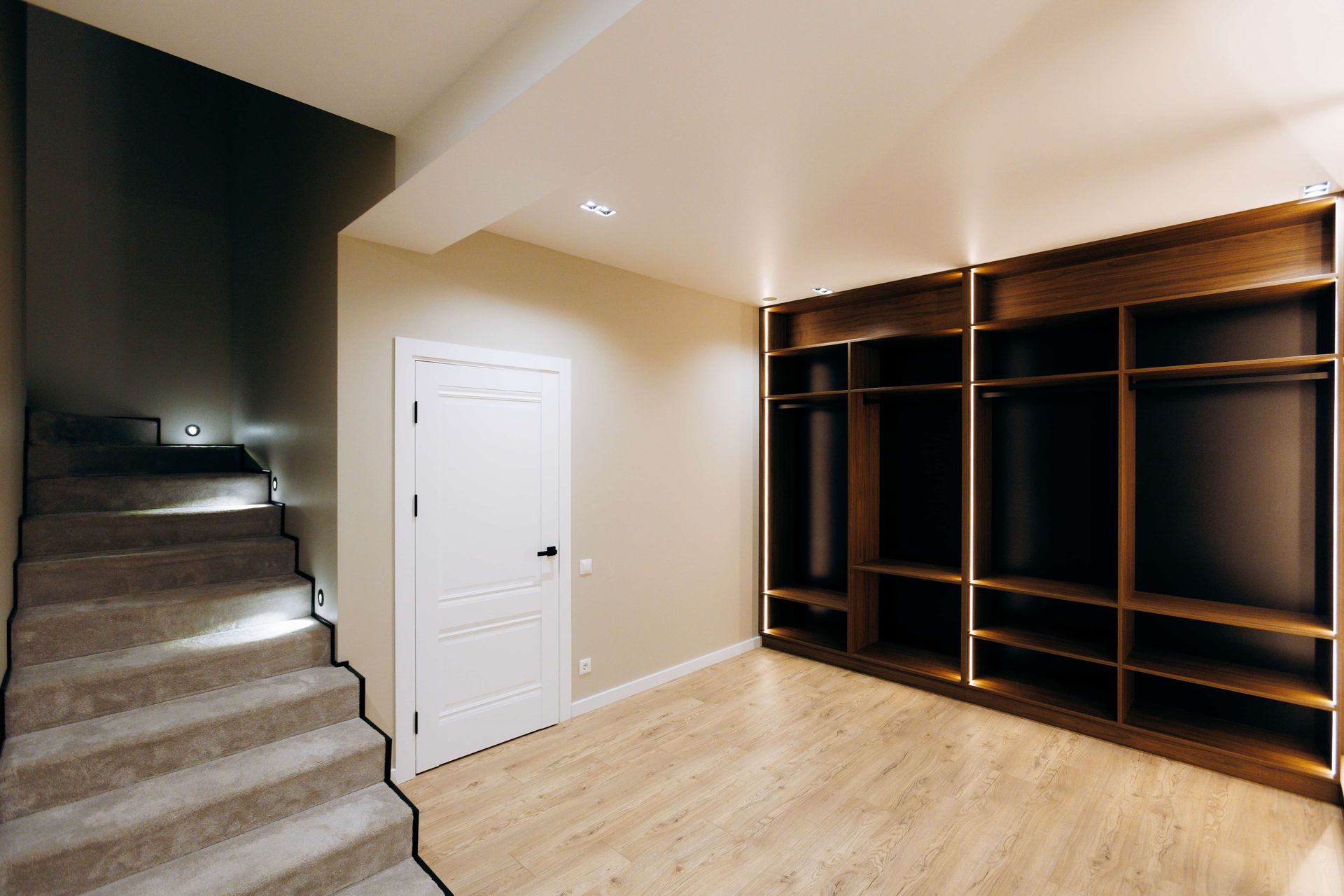 Spacious room with carpeted stairs, white door, and dark wood built-in closets on the right.