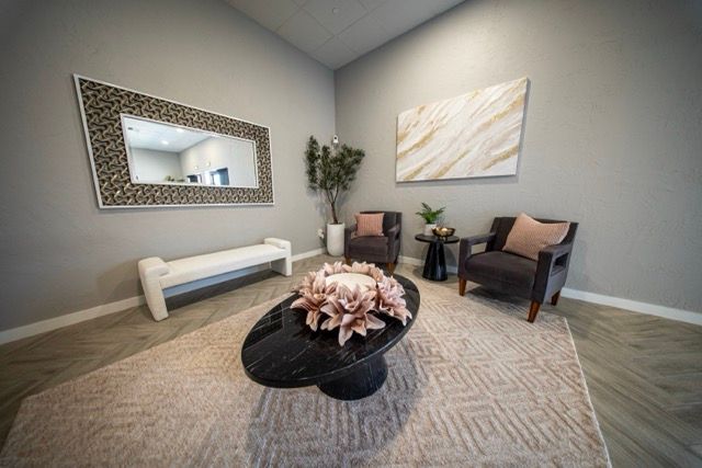 Modern living room with gray walls, a patterned rug, round coffee table, bench, armchair, plants, and wall art