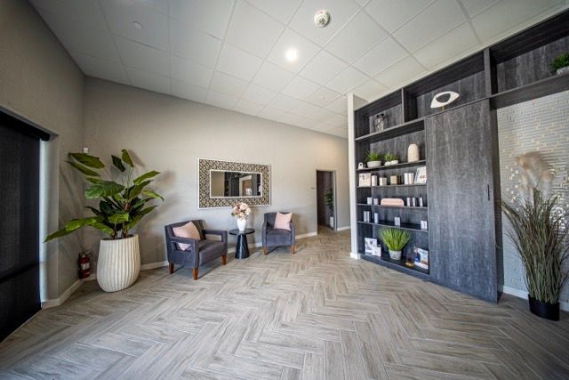 Modern spa room with four cushioned lounge chairs on a wood floor against gray walls.