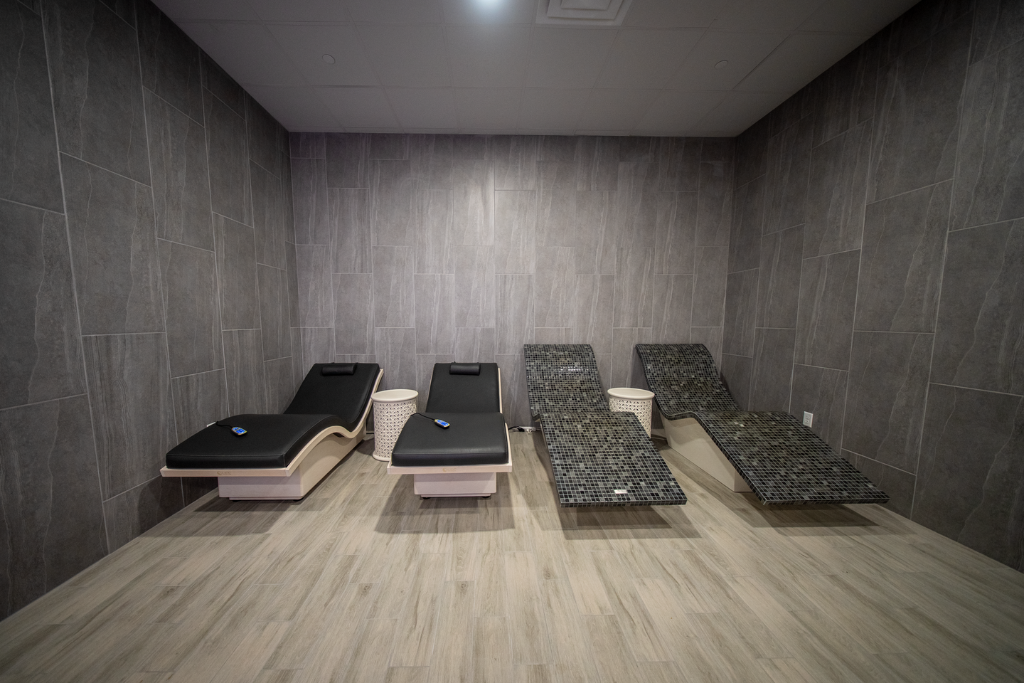 Empty spa room with four padded massage tables against gray walls and a light wood floor