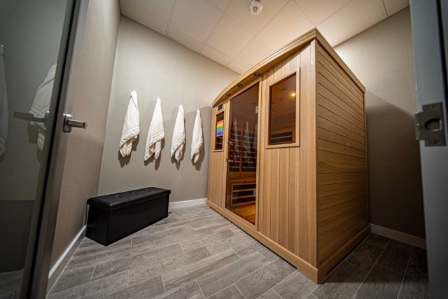 Wood-paneled sauna in a modern changing room with towels on the wall and a black bench.
