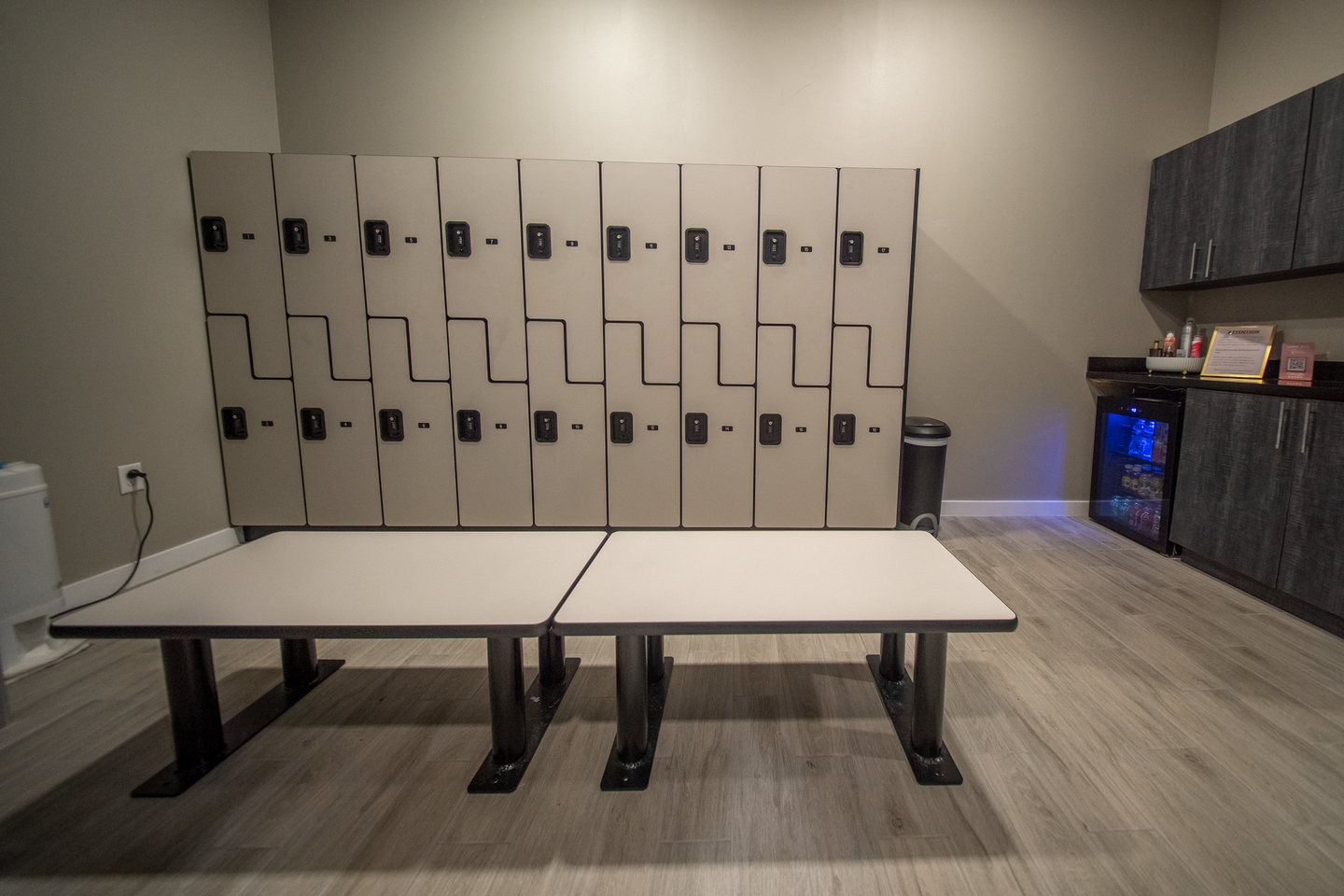 Locker room with beige lockers, two benches, and cabinets along the wall