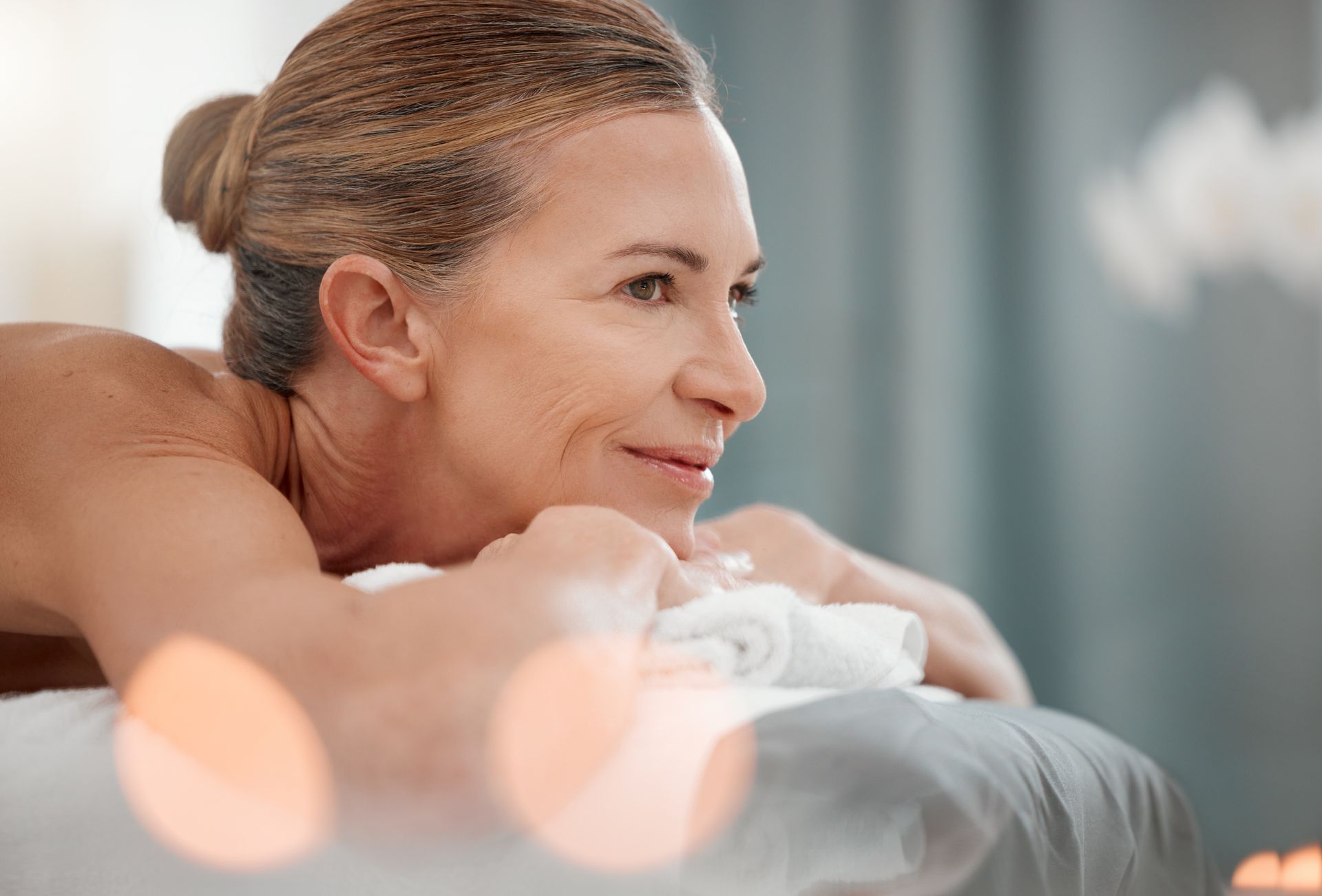 Woman relaxing on massage table, looking peaceful. Soft lighting, blurred foreground.