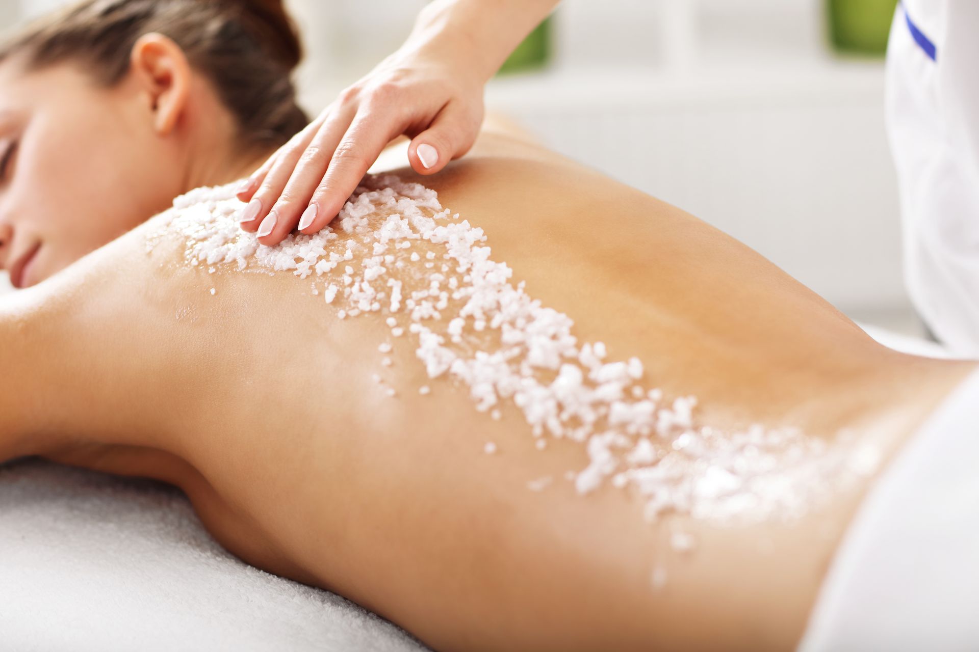 Woman receiving a back scrub at a spa; white scrub applied to her back by a spa worker.