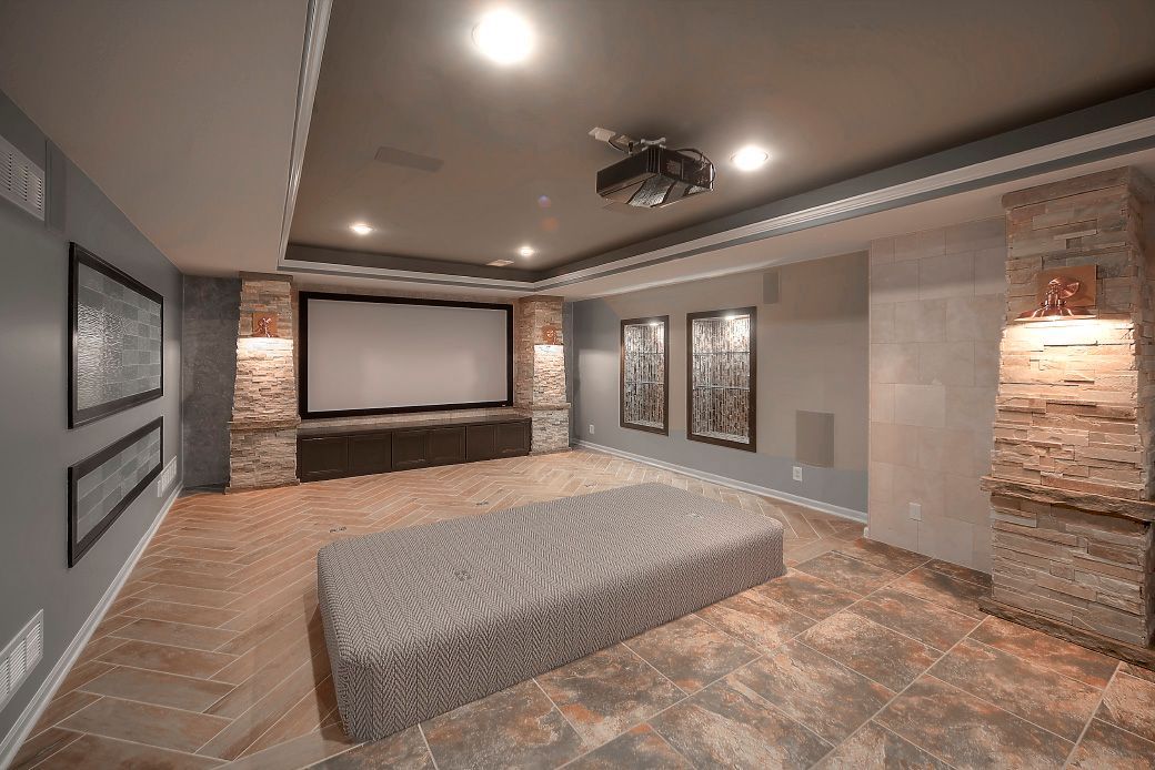 Home theater with a screen, ceiling-mounted projector, stone columns, and a large gray cushioned seating platform.
