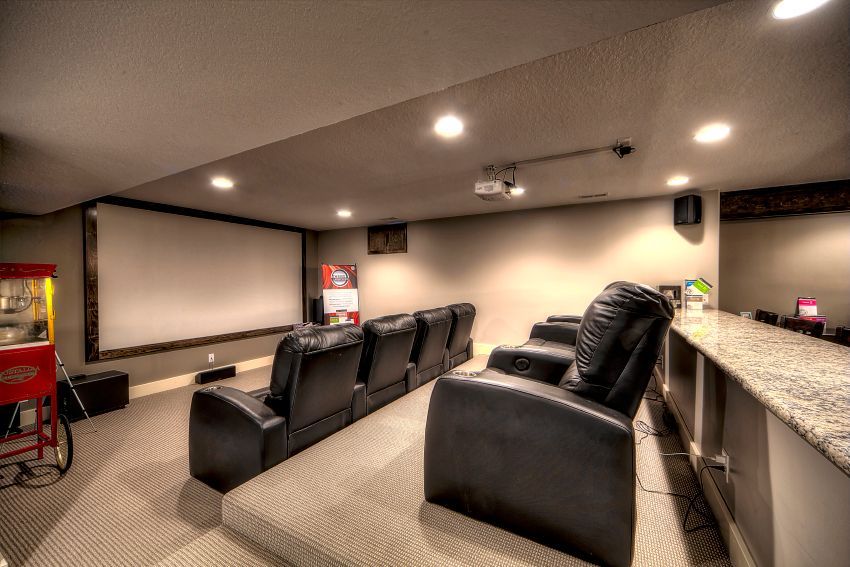 A home theater room with tiered rows of black leather recliners facing a large projector screen and a popcorn machine.