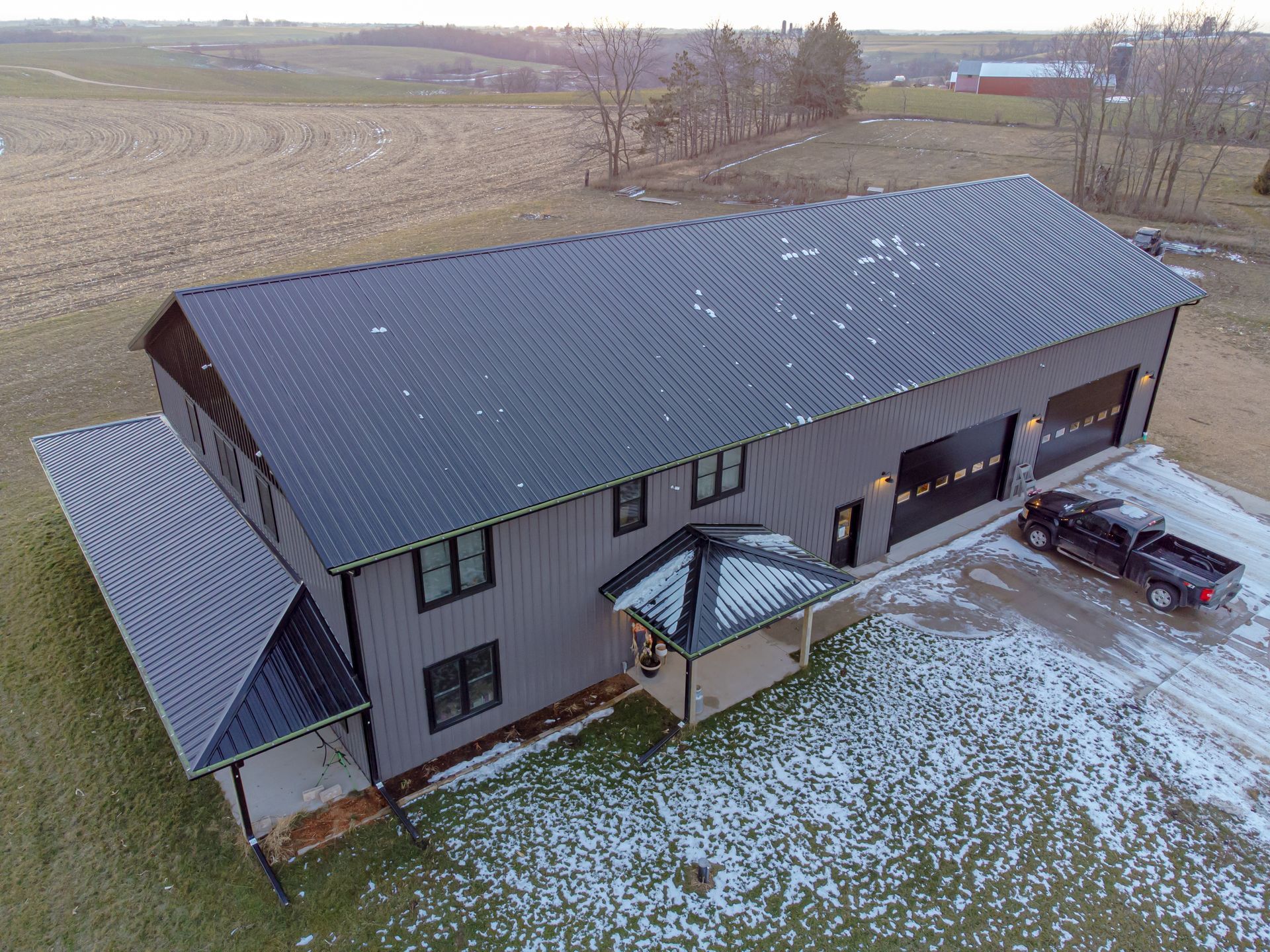 An aerial view of a dark grey metal-sided building with a black roof, featuring two garage doors and a pickup truck nearby.