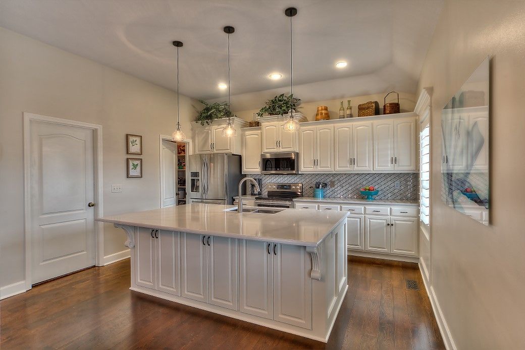 A bright kitchen with white cabinets, a large central island, pendant lights, and hardwood floors.