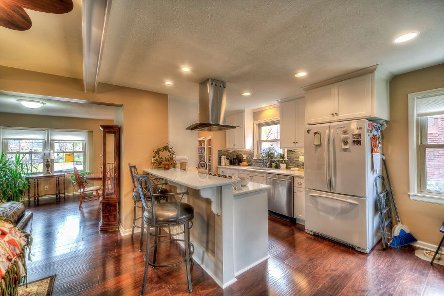 A kitchen with white cabinets, stainless appliances, a central island with bar stools, and warm wood flooring.