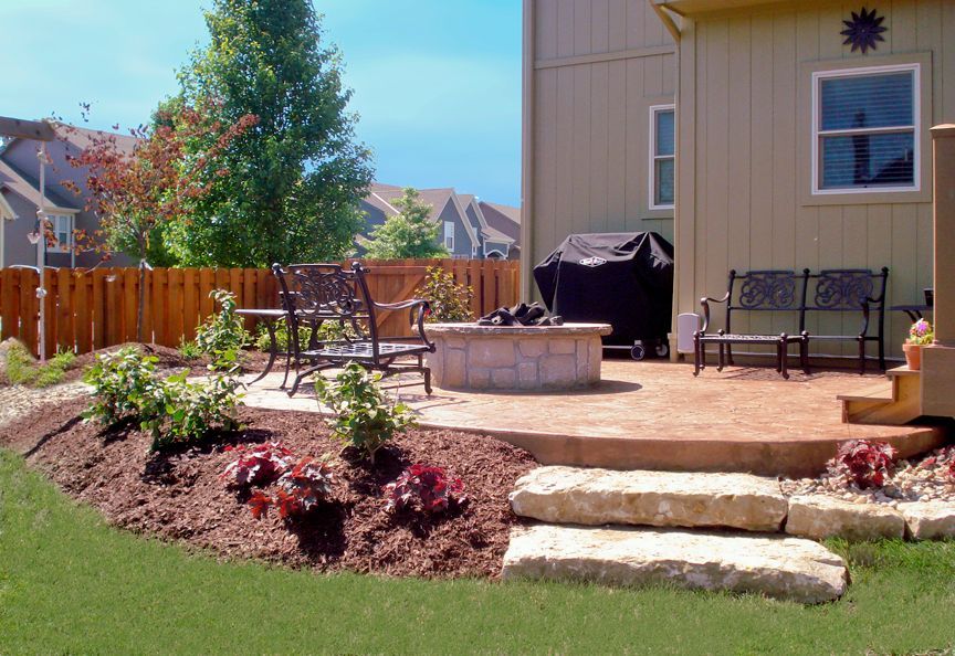 Backyard patio featuring a stone fire pit, outdoor metal seating, a grill, and tiered stone steps leading to a garden bed.