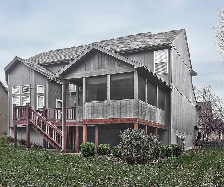 A two-story grey wood-sided house featuring a back deck with stairs and an attached screened-in porch on a grassy lot.