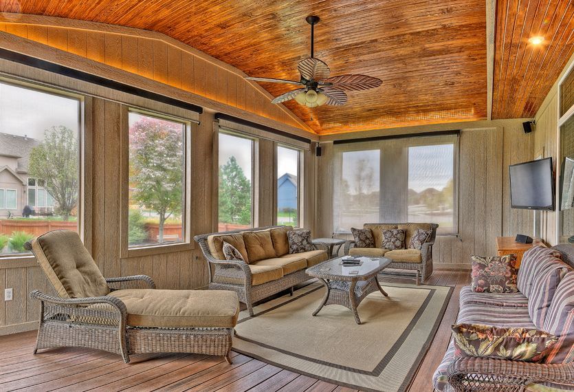 A sunroom with wooden vaulted ceilings, wicker furniture, a neutral rug, and large windows looking out to a yard.