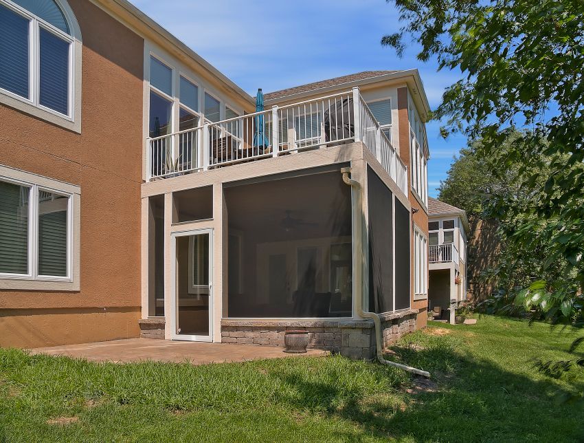 A tan two-story house with a white-framed screened-in porch on the ground level and a balcony deck above it.