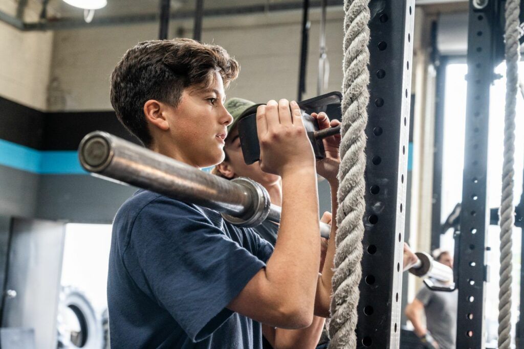 A young boy is lifting a barbell in a gym.