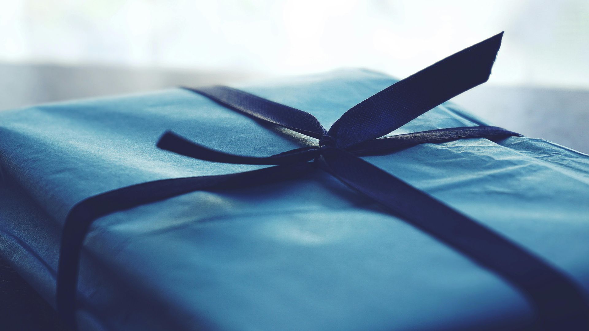 A blue gift wrapped in blue paper with a black ribbon tied around it.