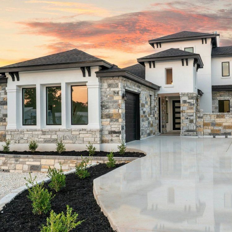 Modern luxury house exterior with stone accents, large windows, and a landscaped driveway at sunset