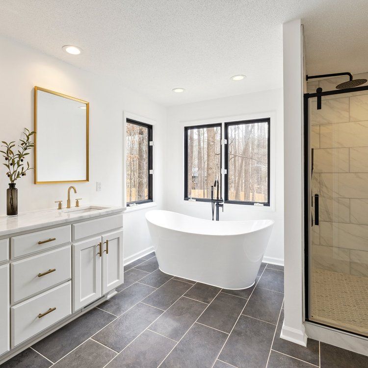 Modern bathroom with white vanity, freestanding tub, dark tile floor, and glass shower