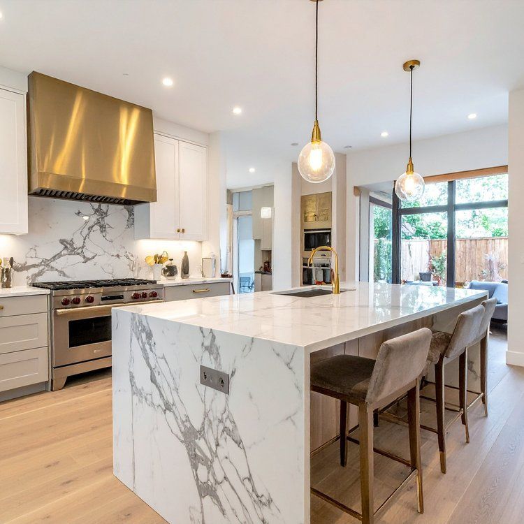Modern kitchen with a marble island, brass pendant lights, and large windows opening to a patio