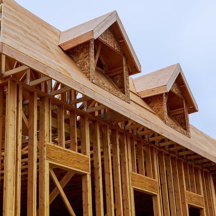 Wood-framed house under construction with exposed plywood walls and roof dormers