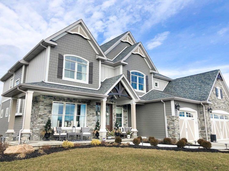 Large gray suburban house with stone accents, gabled rooflines, and a covered front porch on a clear day