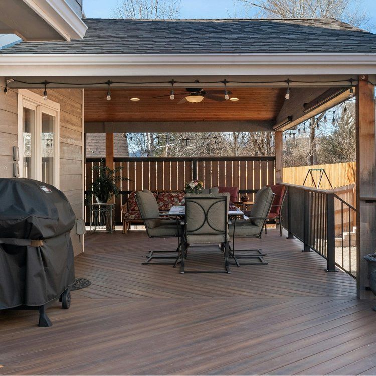 Covered wooden backyard deck with grill, dining table, and black railing