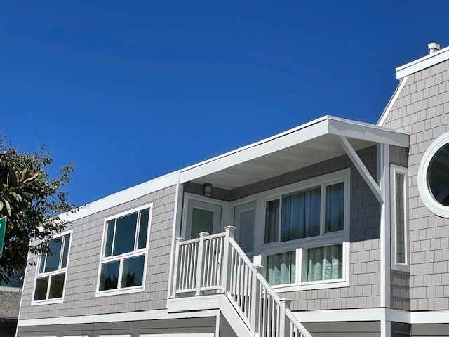 White coastal house with blue trim and balcony under a bright blue sky