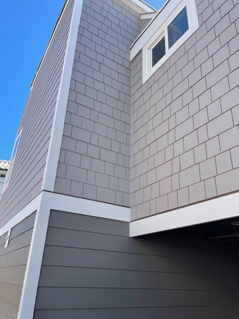 Corner of a gray-shingled house with white trim against a blue sky