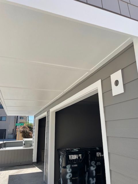 Covered outdoor walkway beside a building, with white ceiling panels and a dark open doorway.