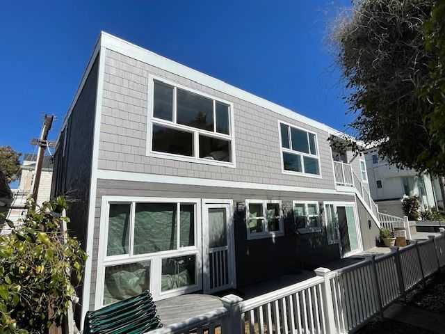 Two-story gray house with white trim and large windows under a clear blue sky
