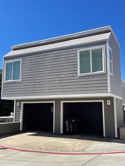 Gray two-story garage apartment with white trim and double open garages under a blue sky