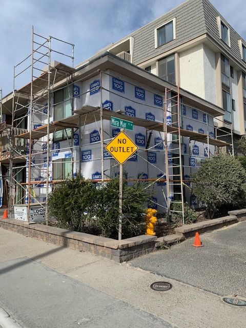 Corner building under construction with scaffolding, blue wrap, and yellow