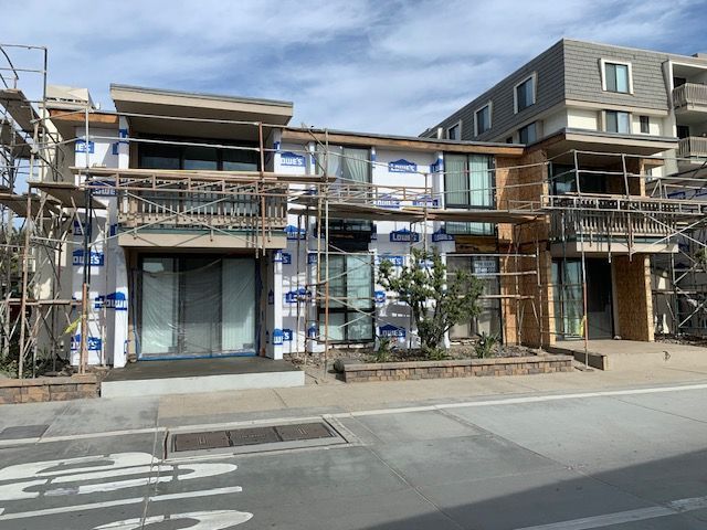 Row of modern townhouses with balconies on a quiet street, covered in scaffolding for construction work