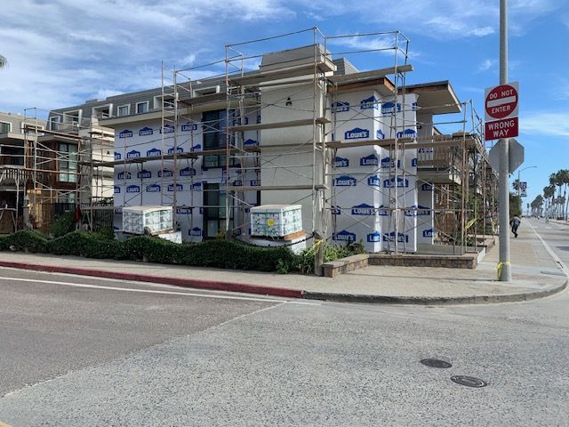 Partially wrapped apartment building at a street corner with construction scaffolding and road signs