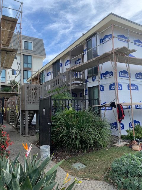 Scaffolding around a building under construction, with wrapped exterior walls and landscaping in front