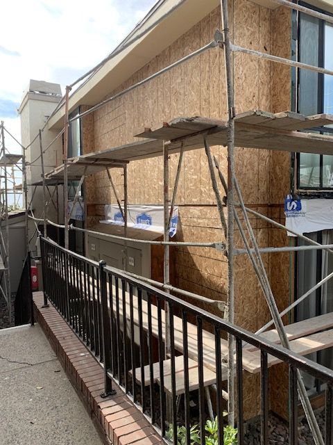 Narrow alley with scaffolding around a tan building beside a black railing and brick walkway