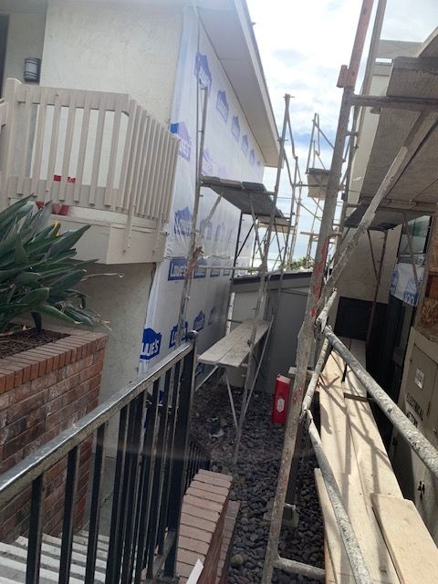 Narrow outdoor alley beside beige buildings, with scaffolding and a red bin between them.