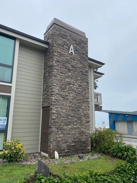 Stone apartment building entrance tower marked “A” beside a landscaped walkway