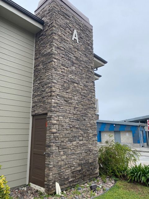 Stone building entrance tower marked “A” beside a beige wall and blue-roofed structure.