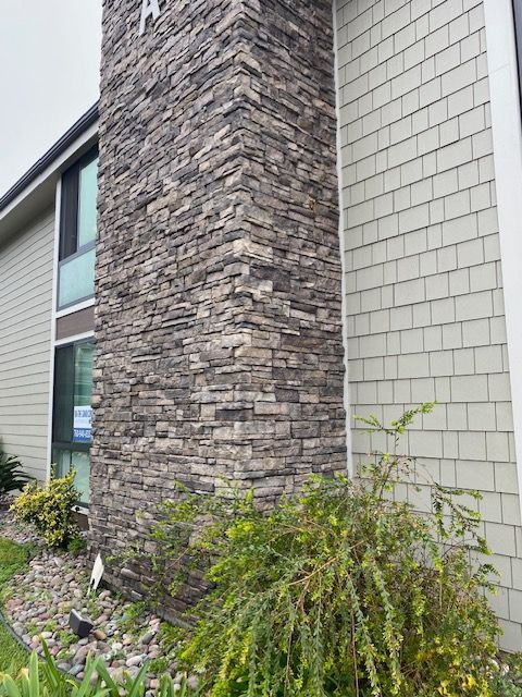Stone and beige house exterior with a tall stone column and shrubs in front